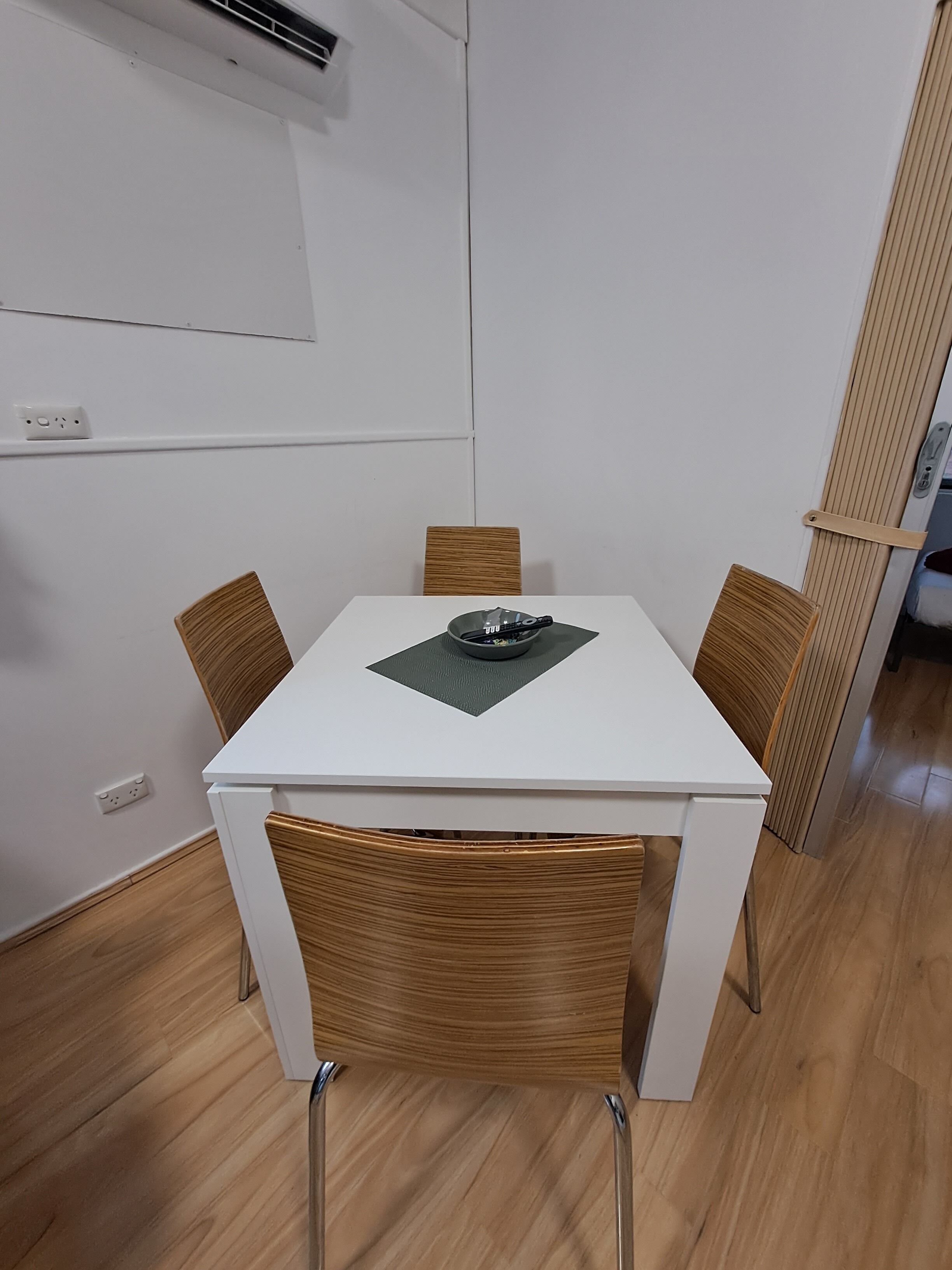 Una mesa de comedor blanca con cuatro sillas, un posavasos negro y suelo de madera.
