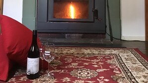 A room with a fireplace, a rug, a bottle of wine, and a glass. - Rosedale Cottages (Taranna)