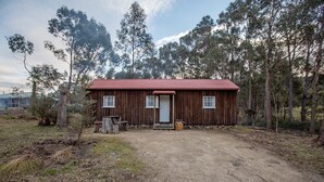A rustic wooden cabin with a red roof, a front door, and a small porch area. - Rosedale Cottages (Taranna)