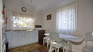 A kitchen with white cabinets, a stove, and a dining table with white chairs. - Rosedale Cottages (Taranna)