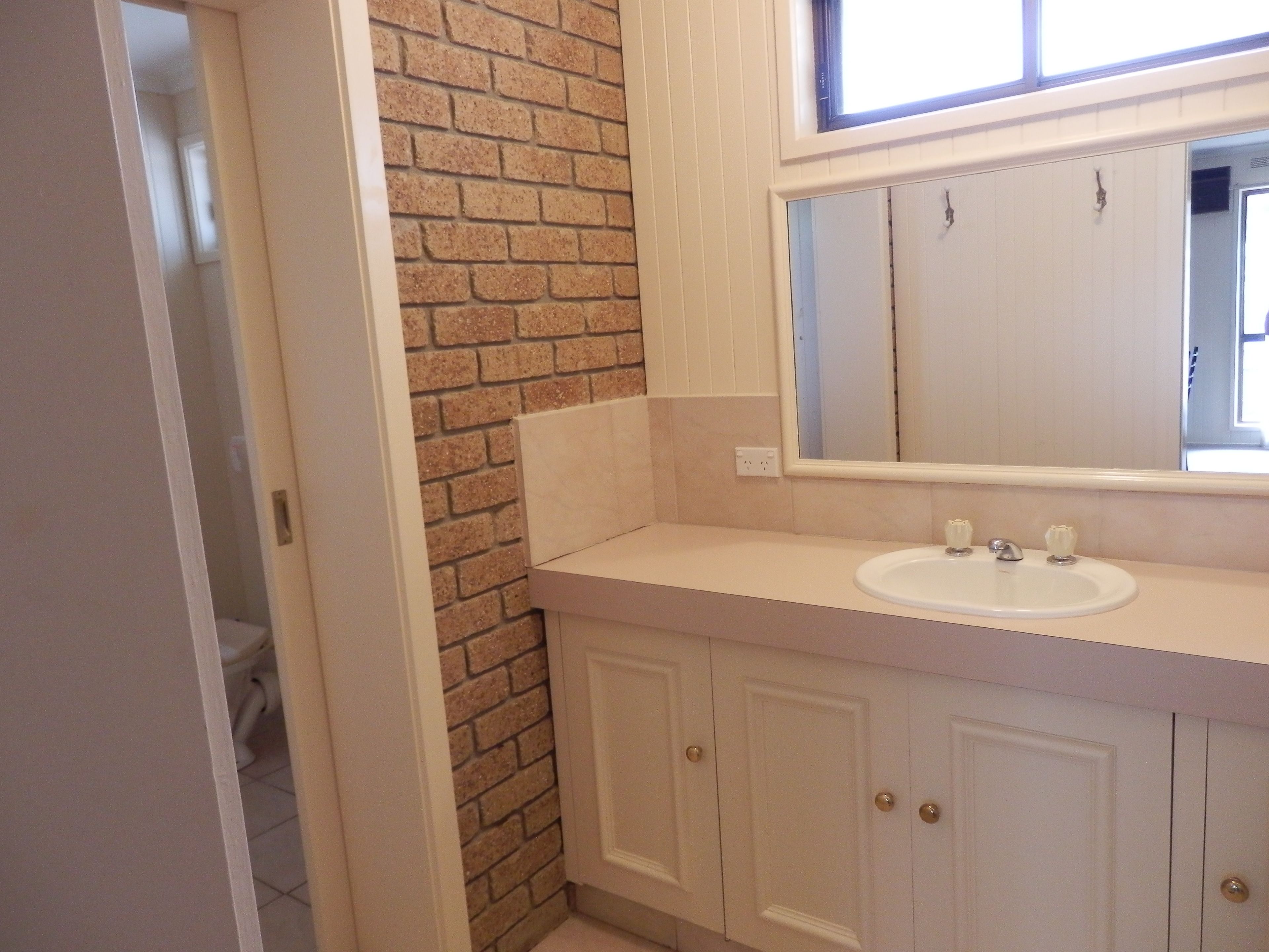 A bathroom with a white sink, a mirror, and a brick accent wall.
