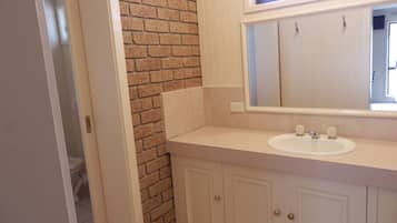 A bathroom with a white sink, a mirror, and a brick accent wall.