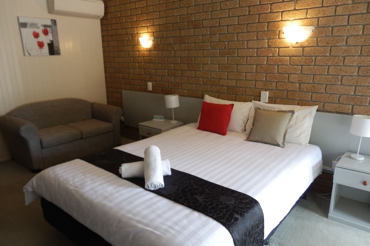 A hotel room with a bed, a sofa, and a brick wall.