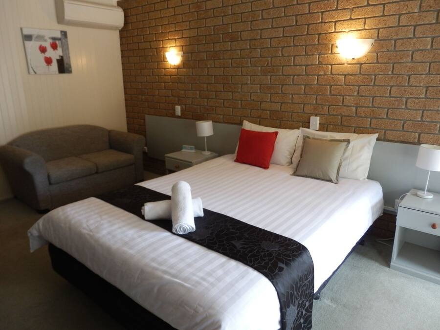 A hotel room with a bed, a sofa, and a brick wall.