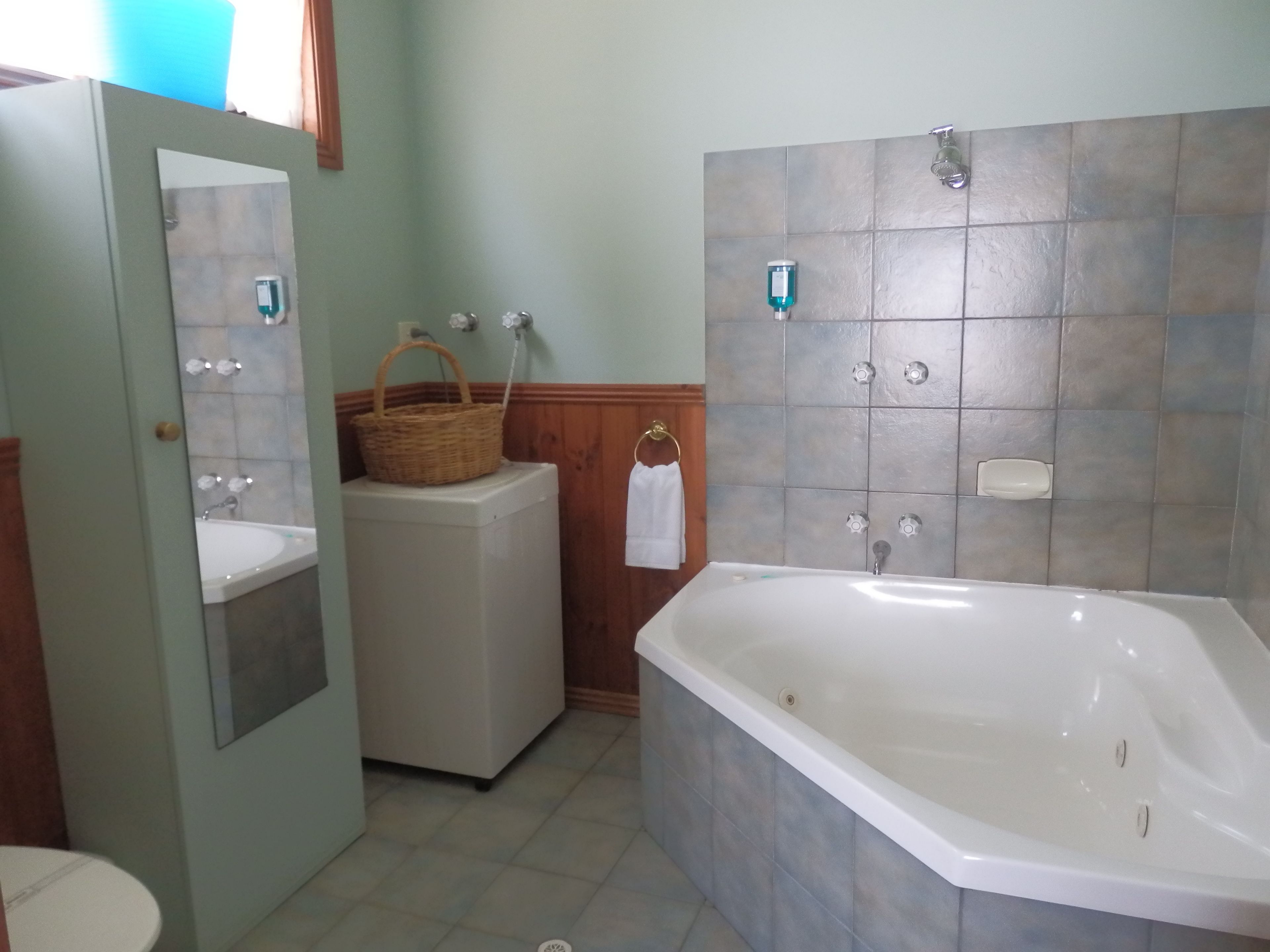 A bathroom with a bathtub, a sink, a washing machine, and a mirror.