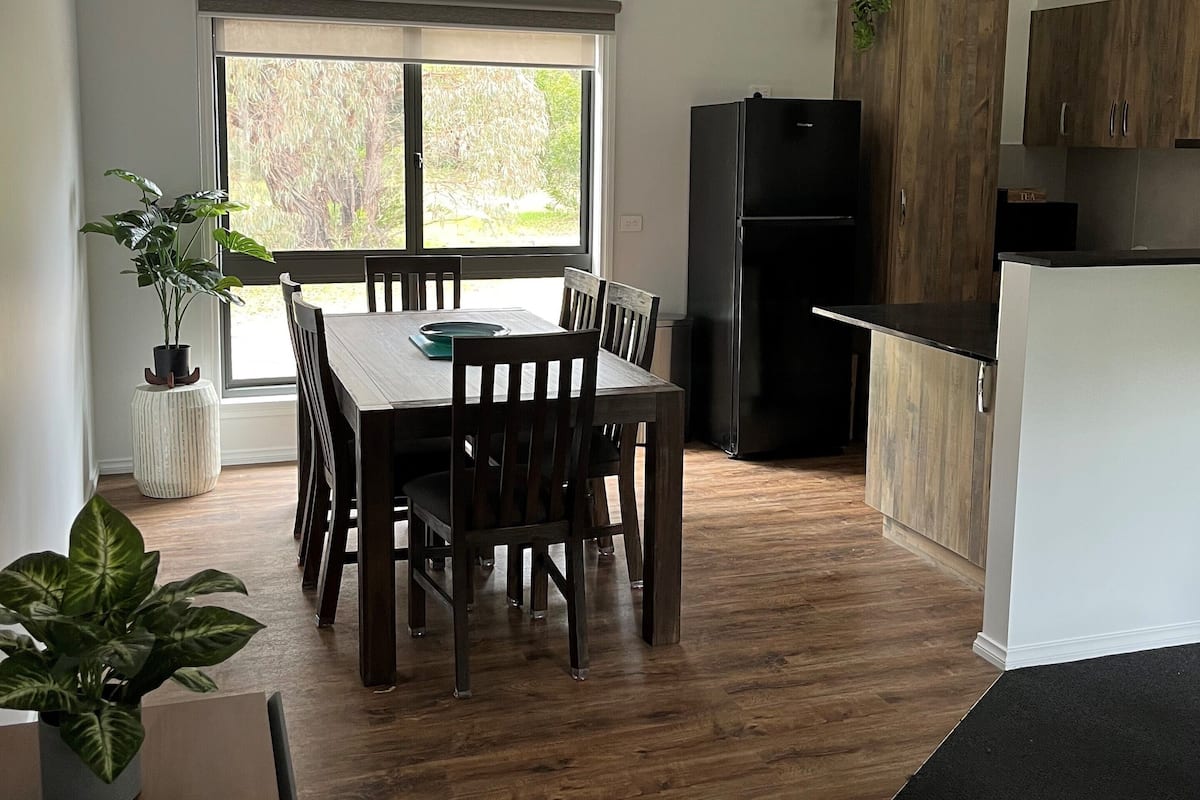 A modern kitchen with a dining area, wooden flooring, and a large window.