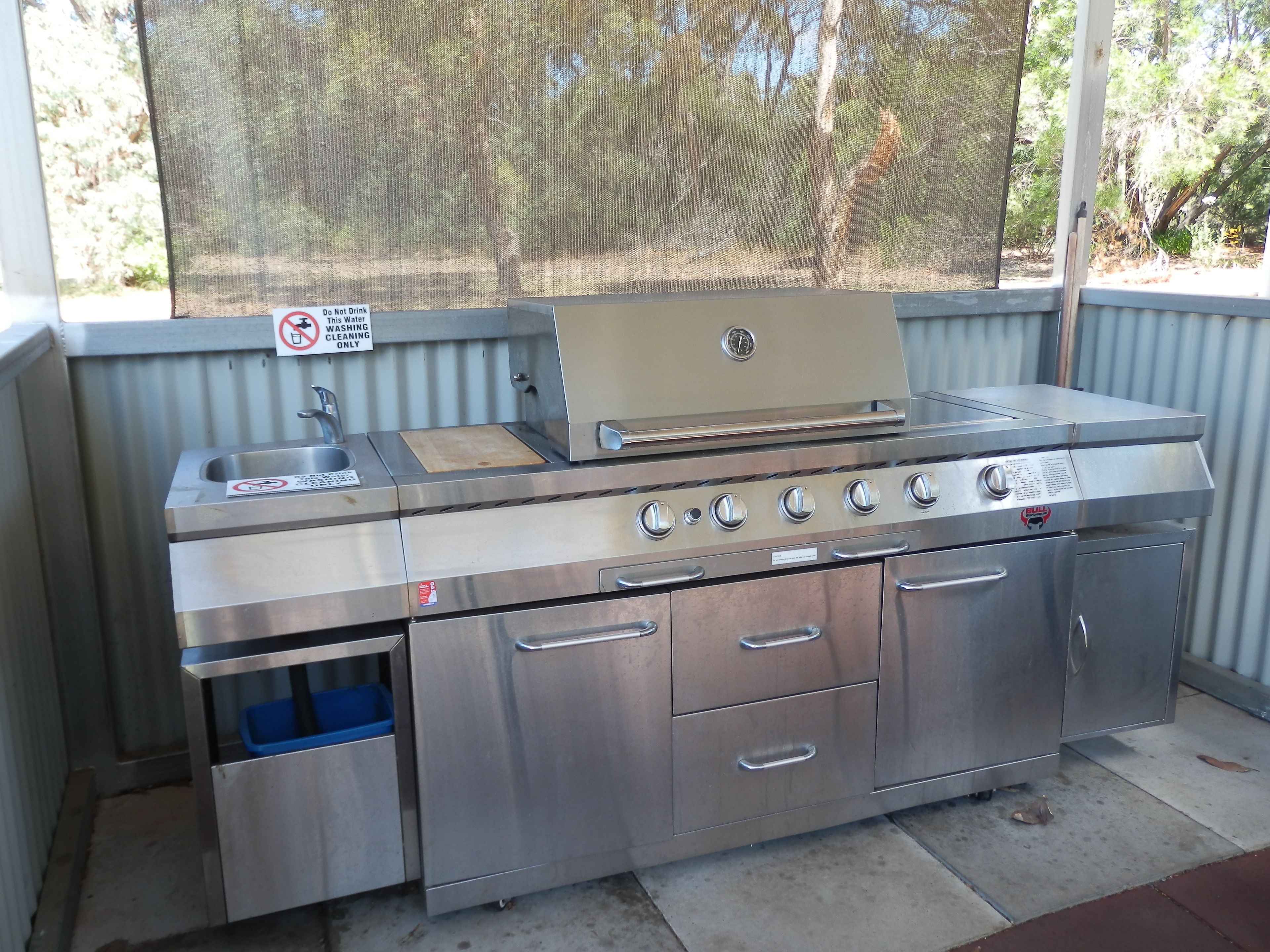 A stainless steel outdoor kitchen with a sink, a grill, and storage drawers.