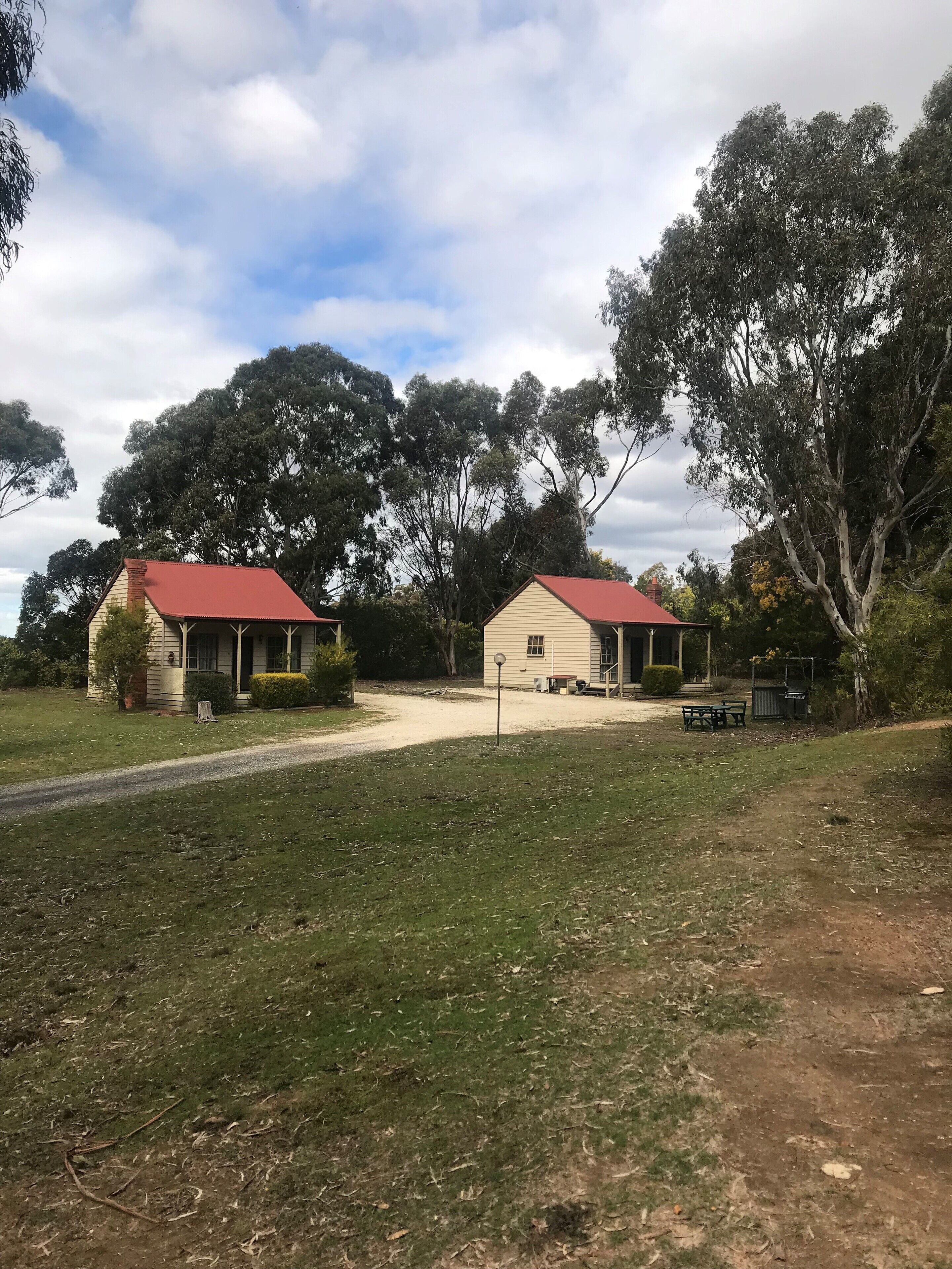 Two small, single-story buildings with red roofs, surrounded by trees and a grassy area.