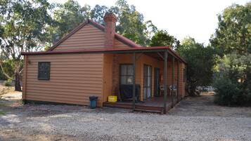 A single-story wooden house with a porch, a chimney, and a gravel driveway.
