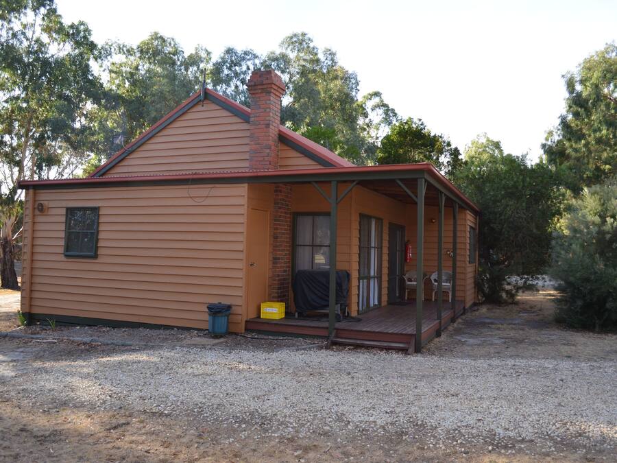 A single-story wooden house with a porch, a chimney, and a gravel driveway.