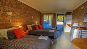 Ein Hotelzimmer mit zwei Betten, einer Küchenzeile, einem Fernseher und einer Schiebetür zum Außenbereich.