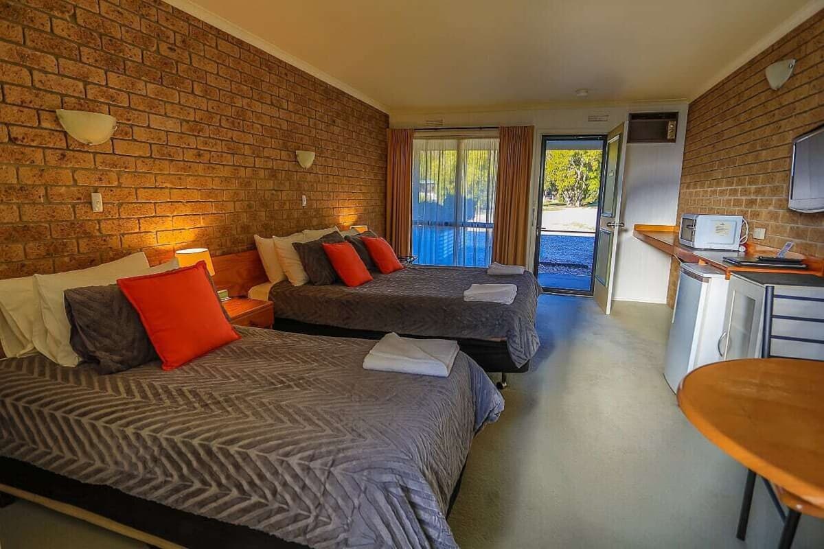 A hotel room with two beds, a kitchenette, a television, and a sliding glass door to the outside.