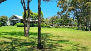 A large, modern building with a white facade and a sloped roof, surrounded by a well-maintained lawn and several trees. - Elfin Hill Country Accommodation (Pokolbin)