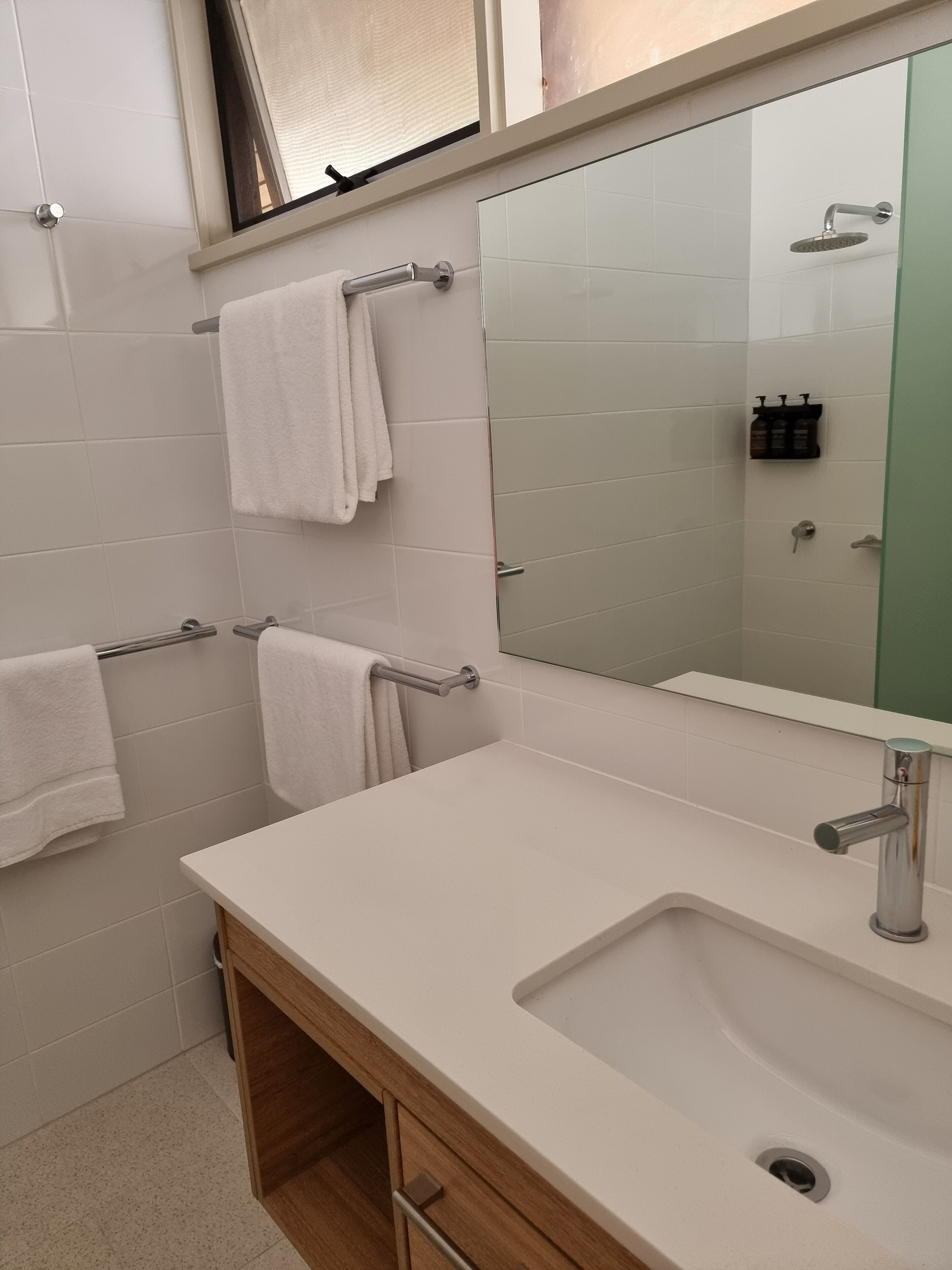 Un baño moderno con azulejos blancos, un espejo grande, un lavabo y toalleros.