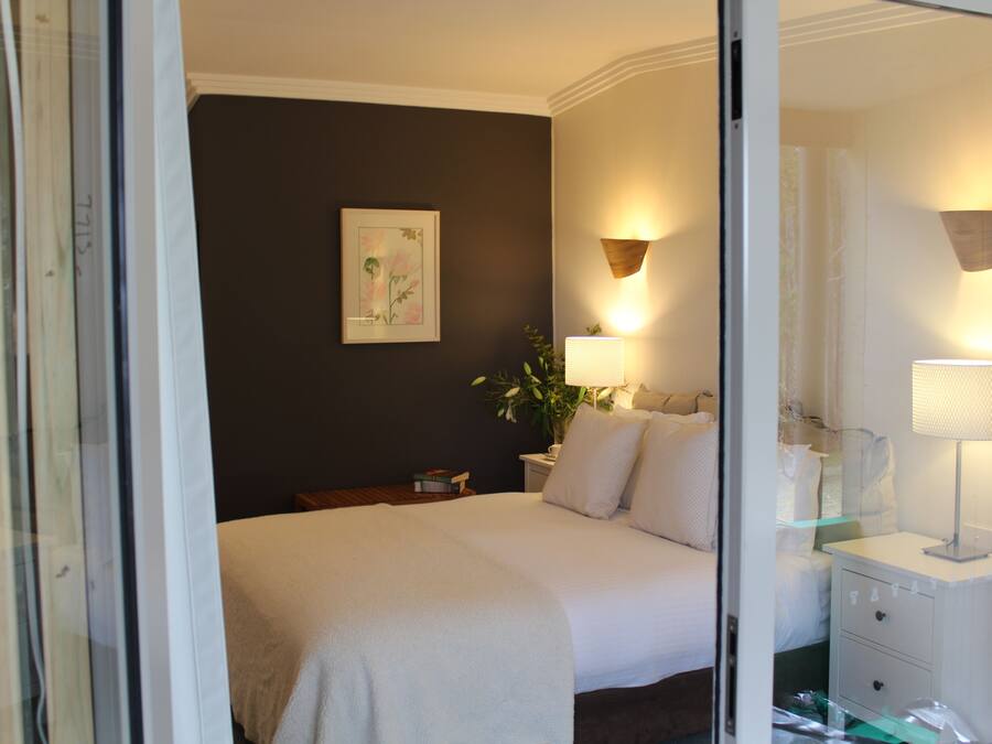 Habitación de hotel con cama, lámparas de noche, mesita de noche, espejo y un cuadro en la pared.