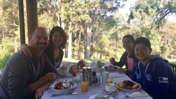 A group of people dining outdoors at a table with various dishes, drinks, and utensils.