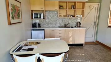 Angolo cottura compatto con zona pranzo, dotato di forno a microonde, lavello e pensili.