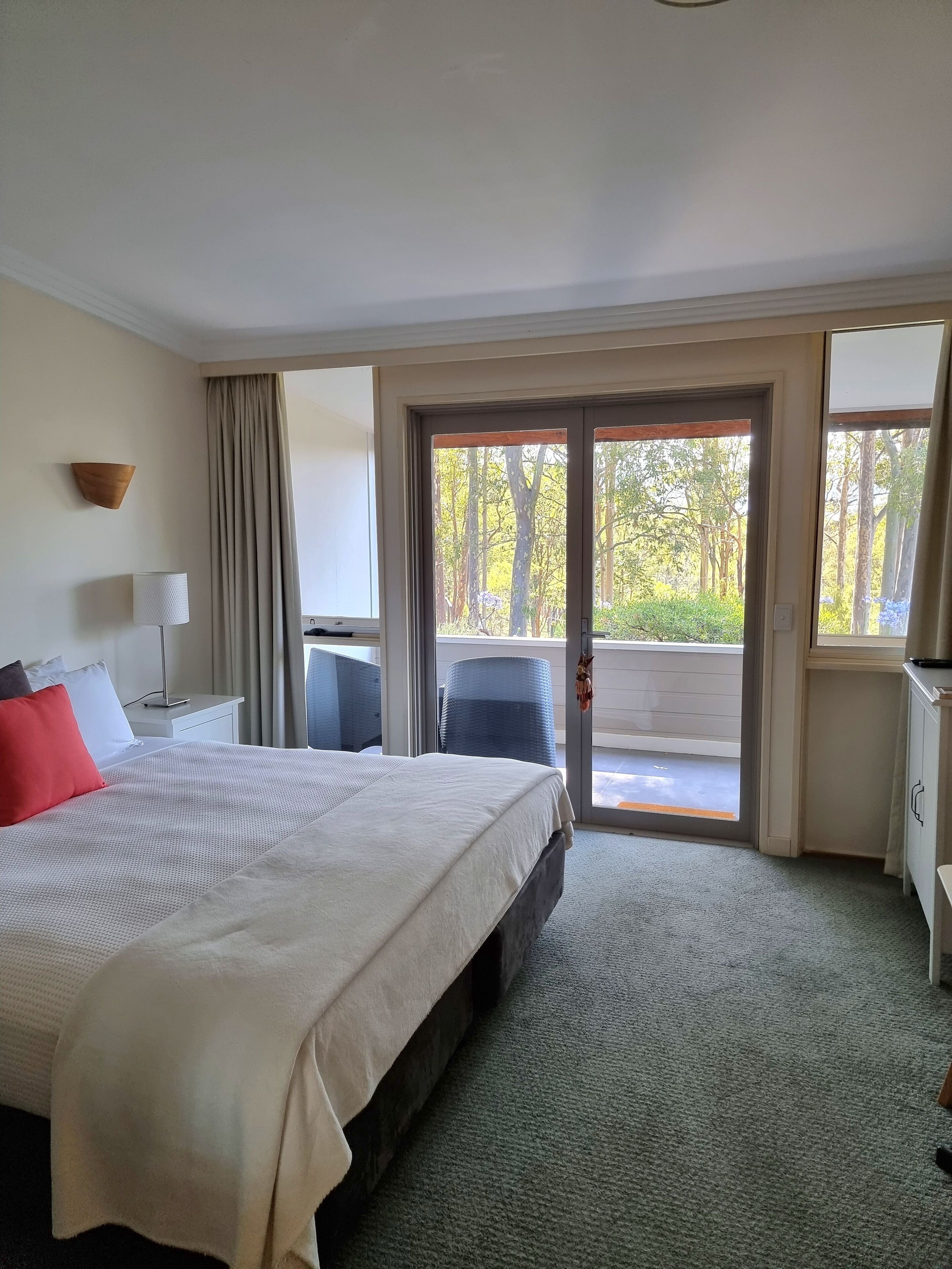 A hotel room with a large bed, a desk, a chair, and a view of the outdoors through a sliding door.