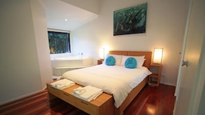 Ein modernes Schlafzimmer mit einem hölzernen Bett, weißen Bettwäsche, zwei blauen Ziertelementen, Nachttischlampen und einem Bild an der Wand.
