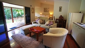 Ein Wohnzimmer mit einer Couch, einem Couchtisch und einem Essbereich mit Tisch und Stühlen. Ein Schiebeglastür führt zu einer Terrasse mit Gartenmöbeln.