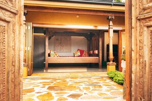 Un banco de madera tradicional con cojines en un patio con suelo de piedra.