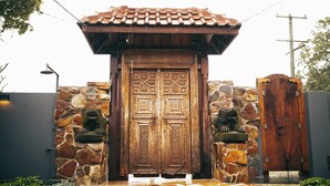 A traditional wooden gate with intricate carvings, flanked by stone walls and two stone lion statues. - Bali at the Bay (Nelson Bay)