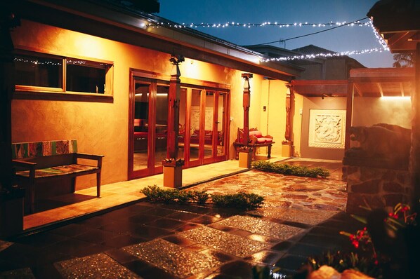 A well-lit patio area with a stone floor, wooden bench, and string lights. - Bali at the Bay (Nelson Bay)