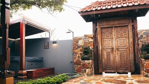 A stone-walled building with a wooden door featuring intricate carvings, a stone bench, and a small garden area with green plants. - Bali at the Bay (Nelson Bay)