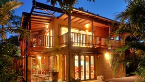 A two-story building with a balcony, a patio with seating, and a well-lit interior. - Bali at the Bay (Nelson Bay)