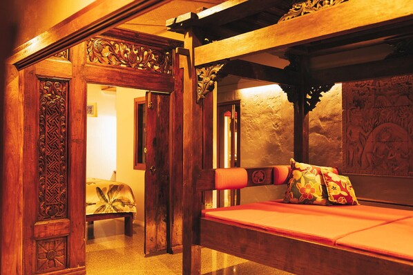 A traditional wooden room with a bed, ornate wooden door, and a stone wall with carvings. - Bali at the Bay (Nelson Bay)