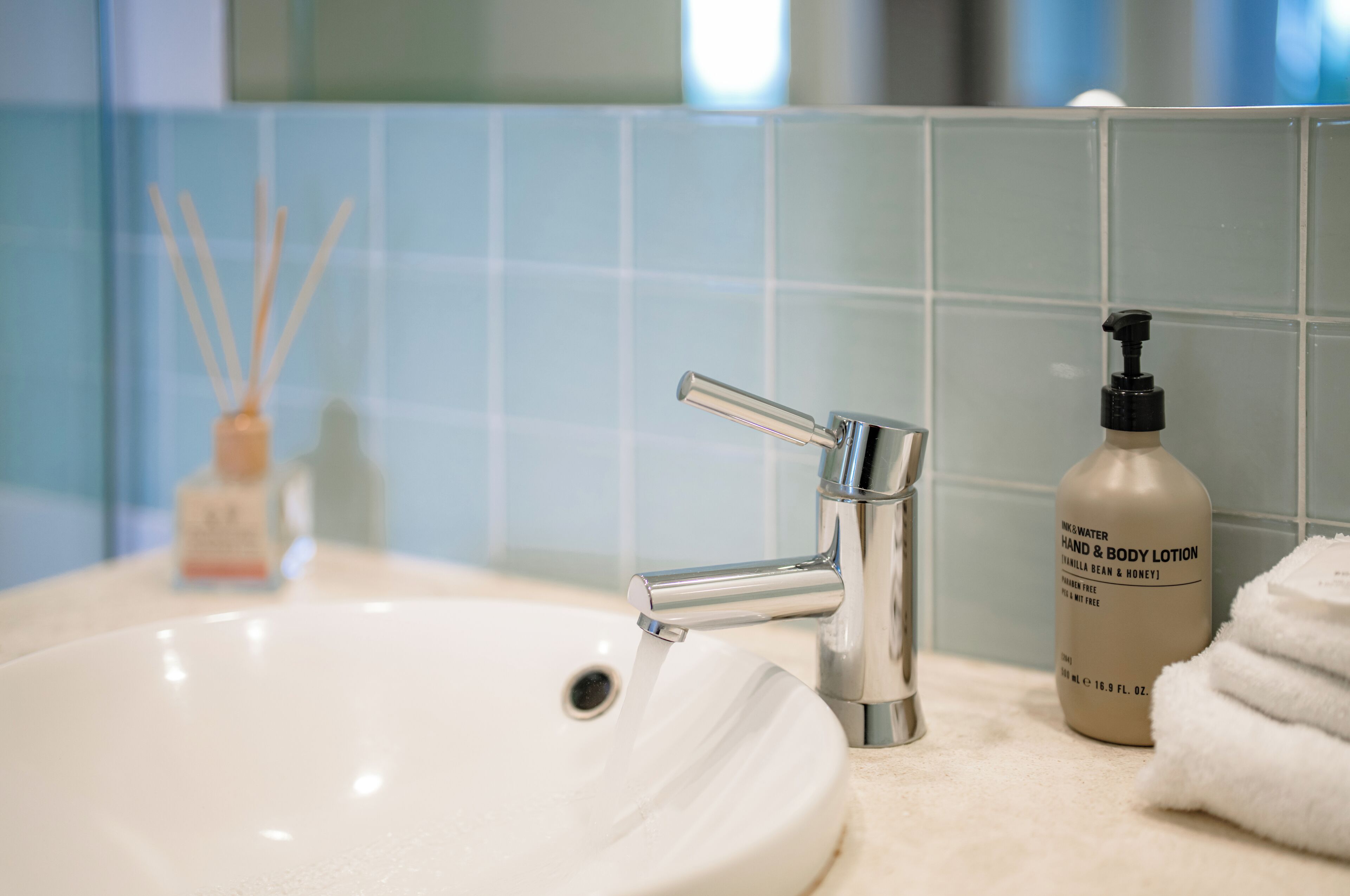Un lavamanos de baño con un grifo moderno, una botella de crema hidratante para manos y cuerpo, y una pila de toallas blancas.