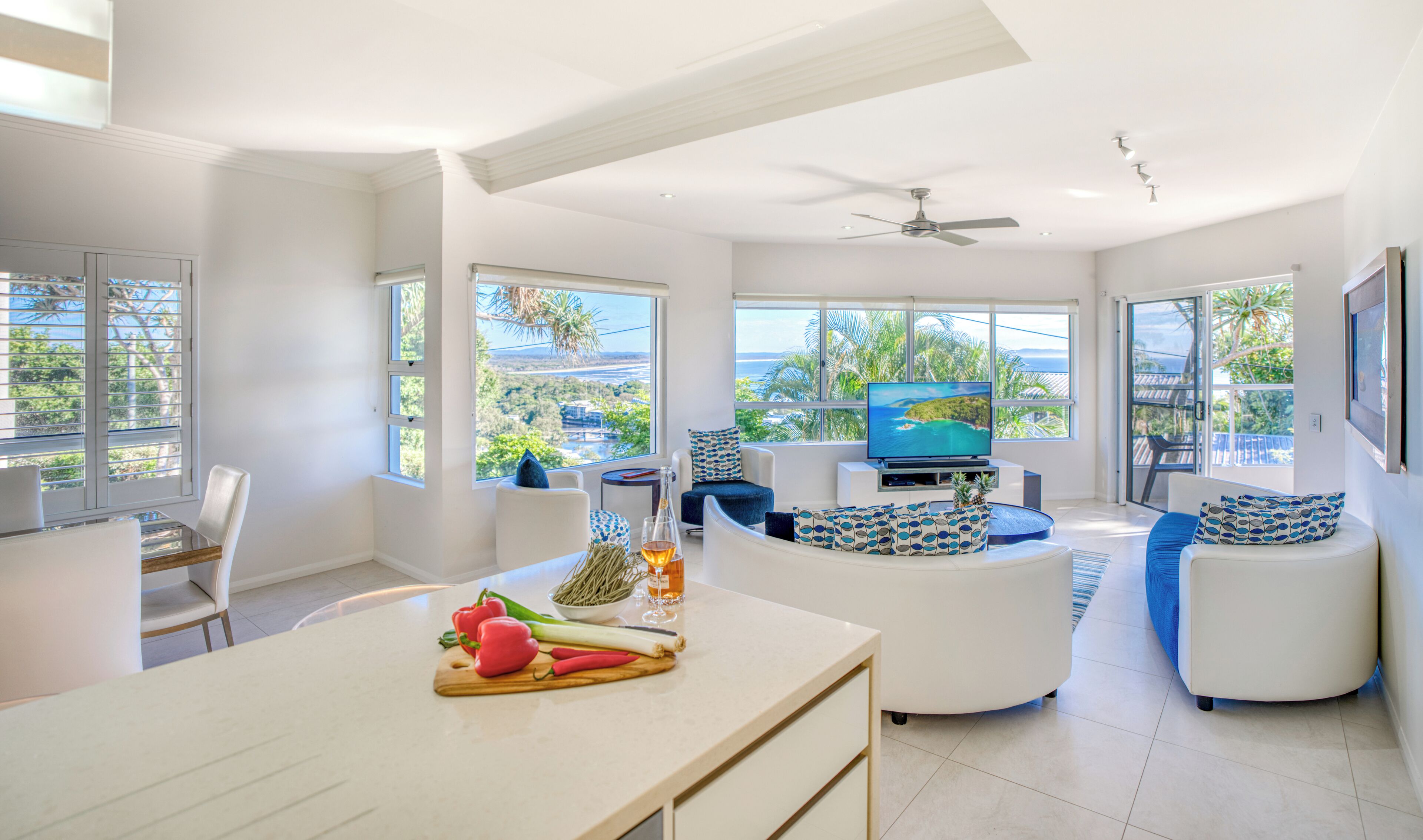 A modern living room with a TV, seating, and a kitchen area with fresh produce.