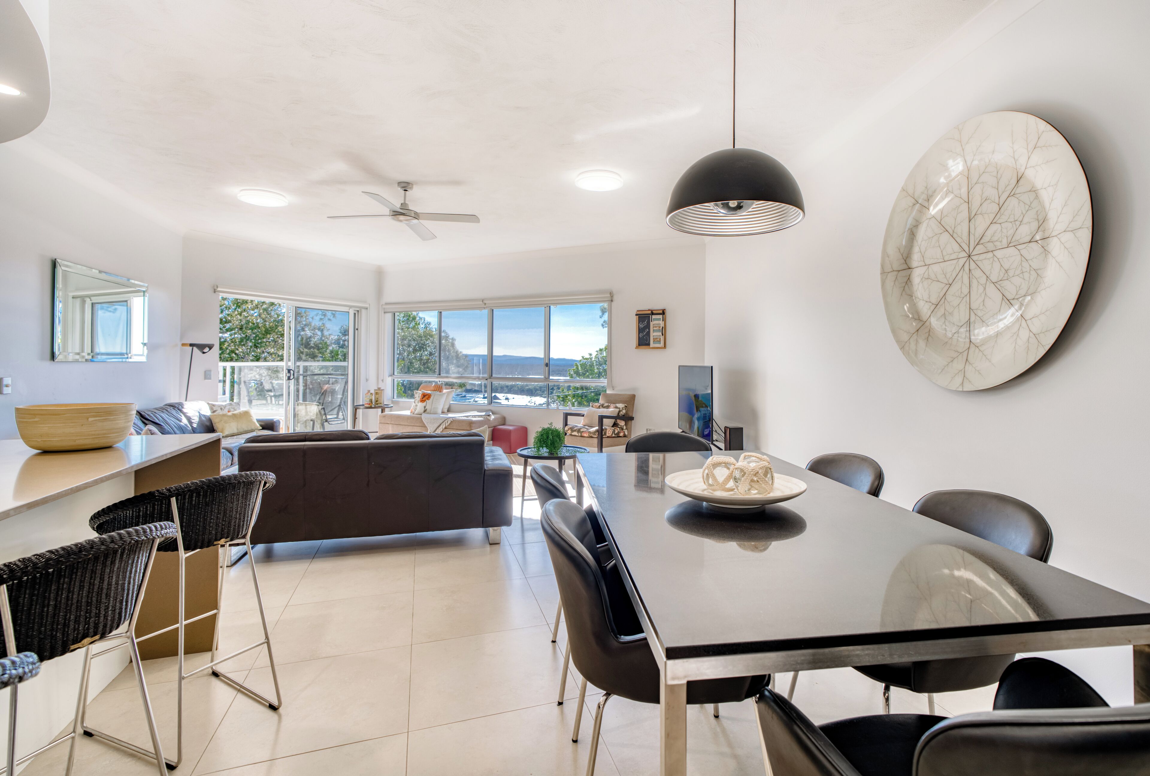 A modern kitchen with a large island, black bar stools, and a dining table with chairs.
