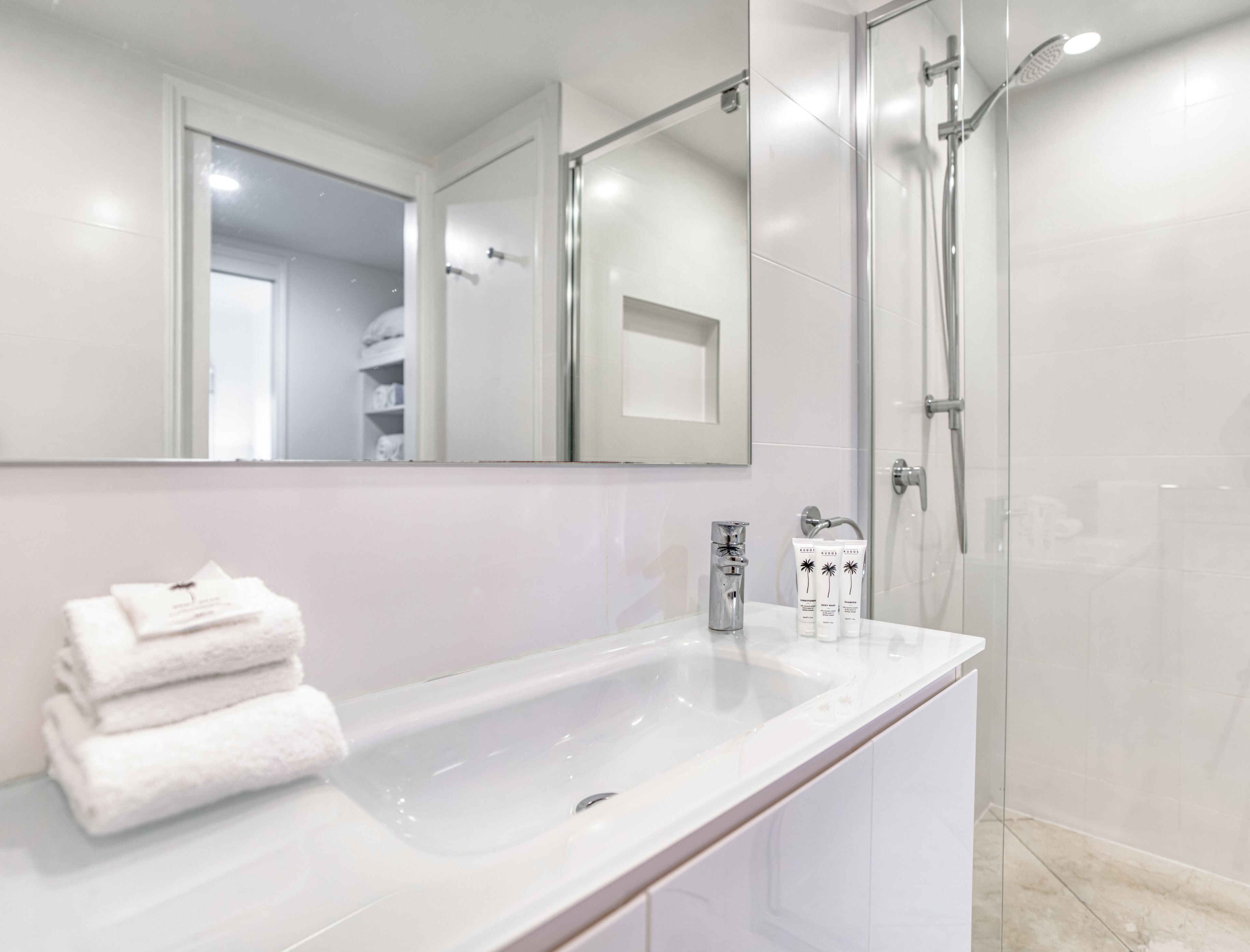 A modern bathroom with a large mirror, a glass shower enclosure, and a white sink with towels.