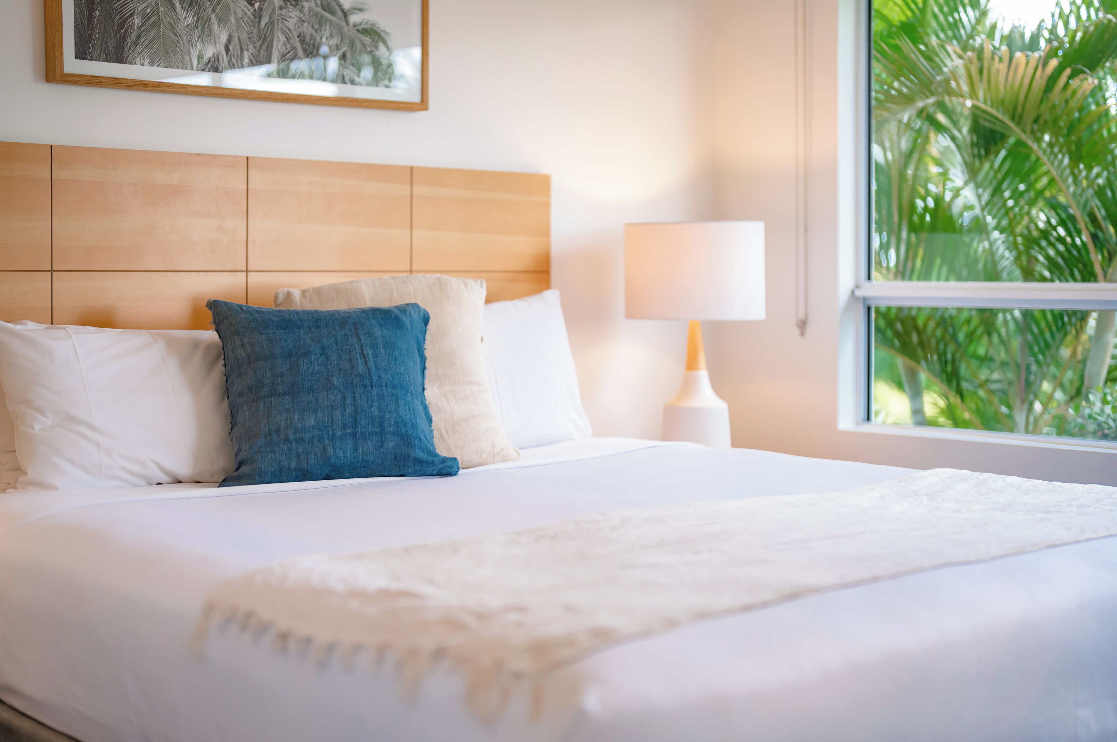 Una cama bien hecha con almohadas blancas y azules, una manta blanca y un cabecero de madera.