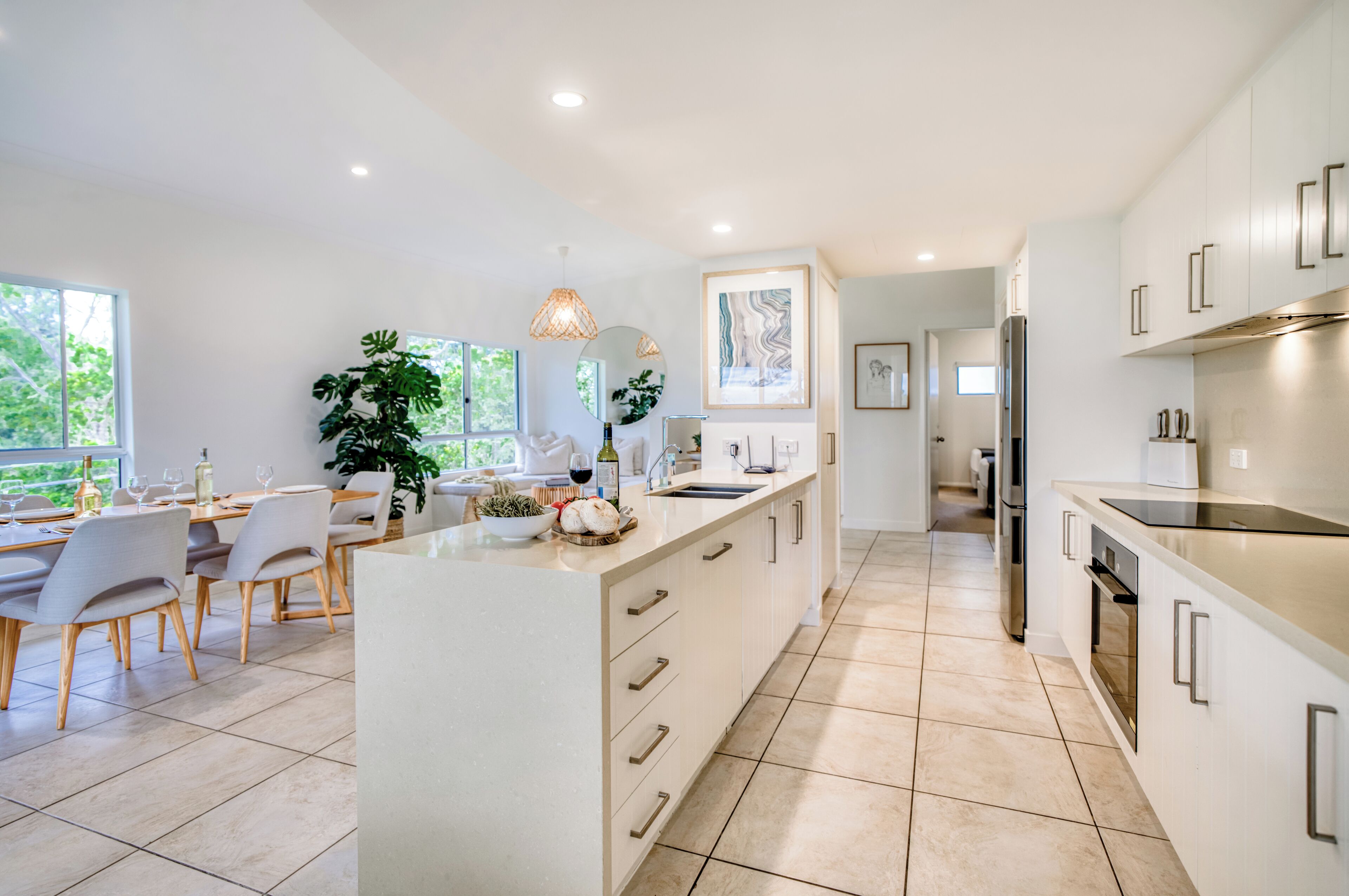 A modern kitchen with white cabinetry, a central island, and a dining area with a table and chairs.