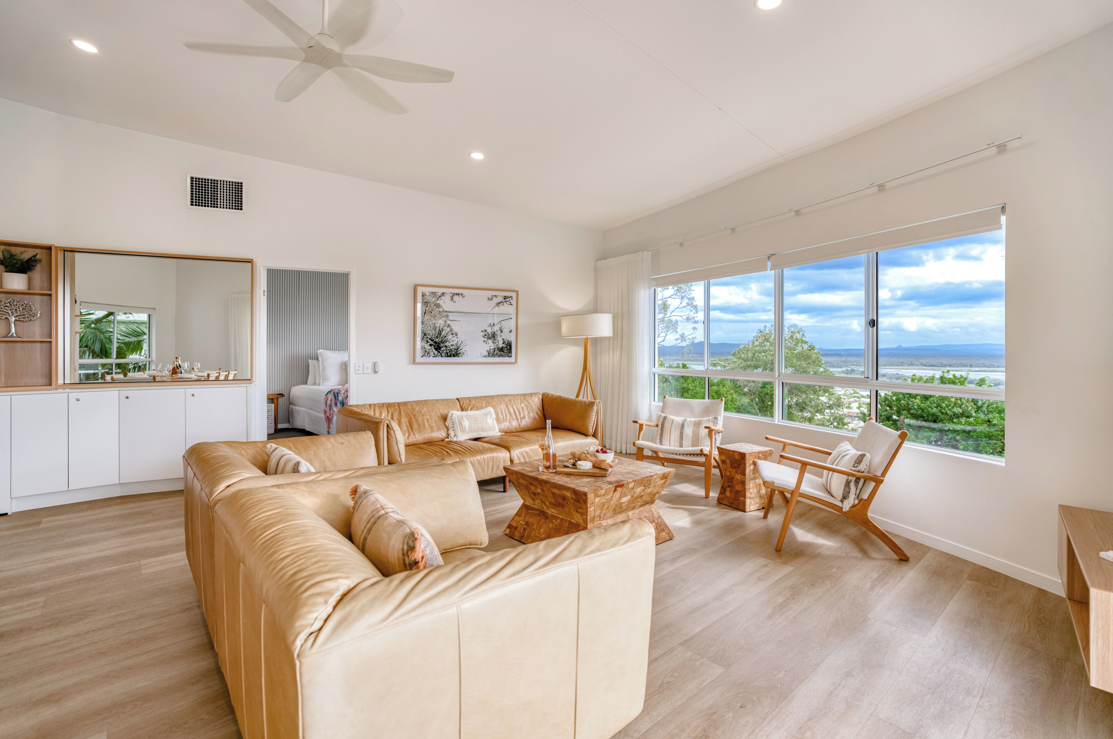 A spacious living area with a large beige sectional sofa, a wooden coffee table, and a view of the outdoors through large windows.