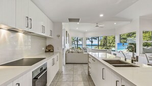 A modern kitchen with white cabinetry, a built-in oven, and a large island with a sink. - The Lookout Resort (Noosa Heads)