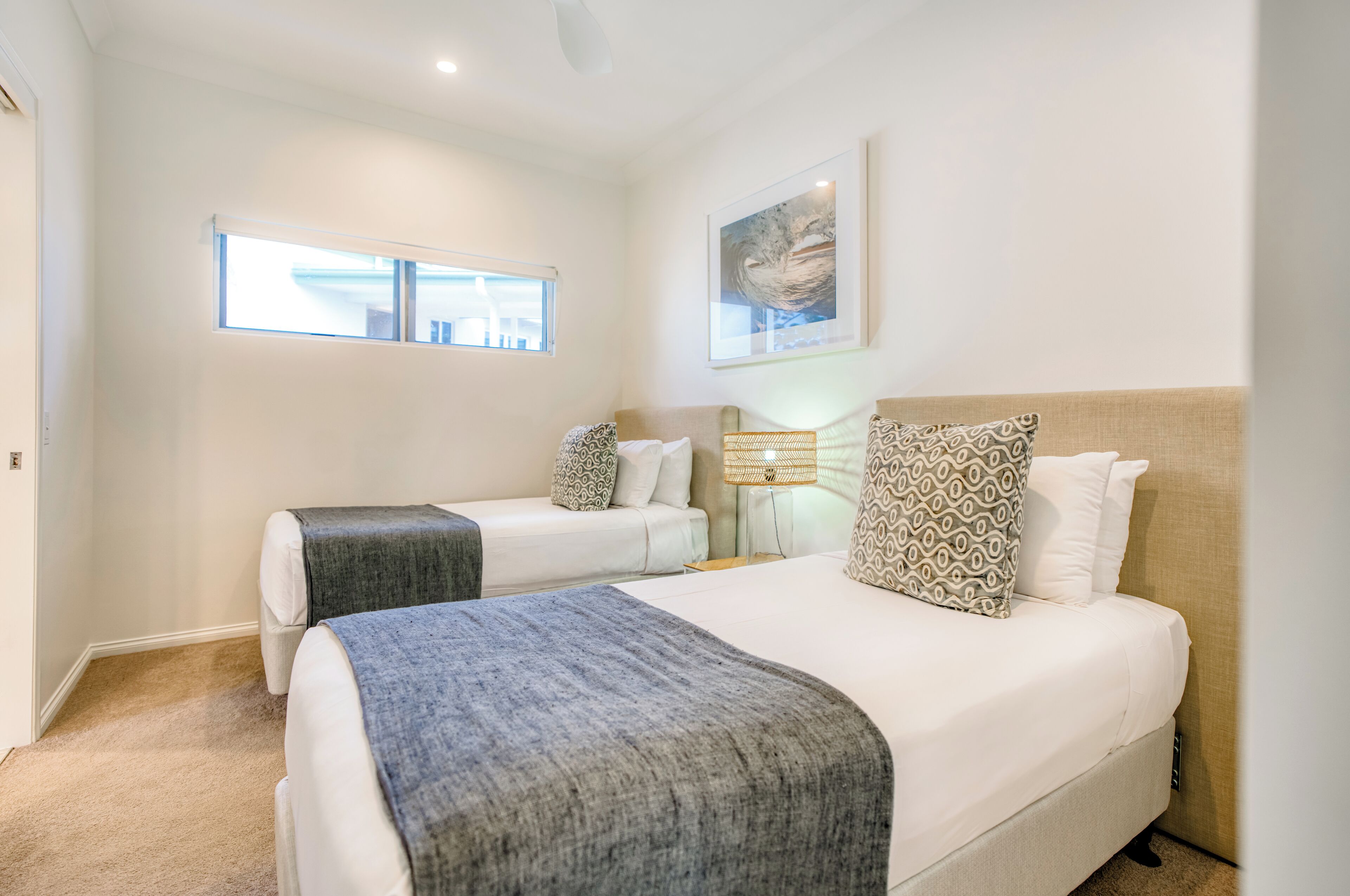 A hotel room with two beds, a window, a ceiling fan, and a painting on the wall.