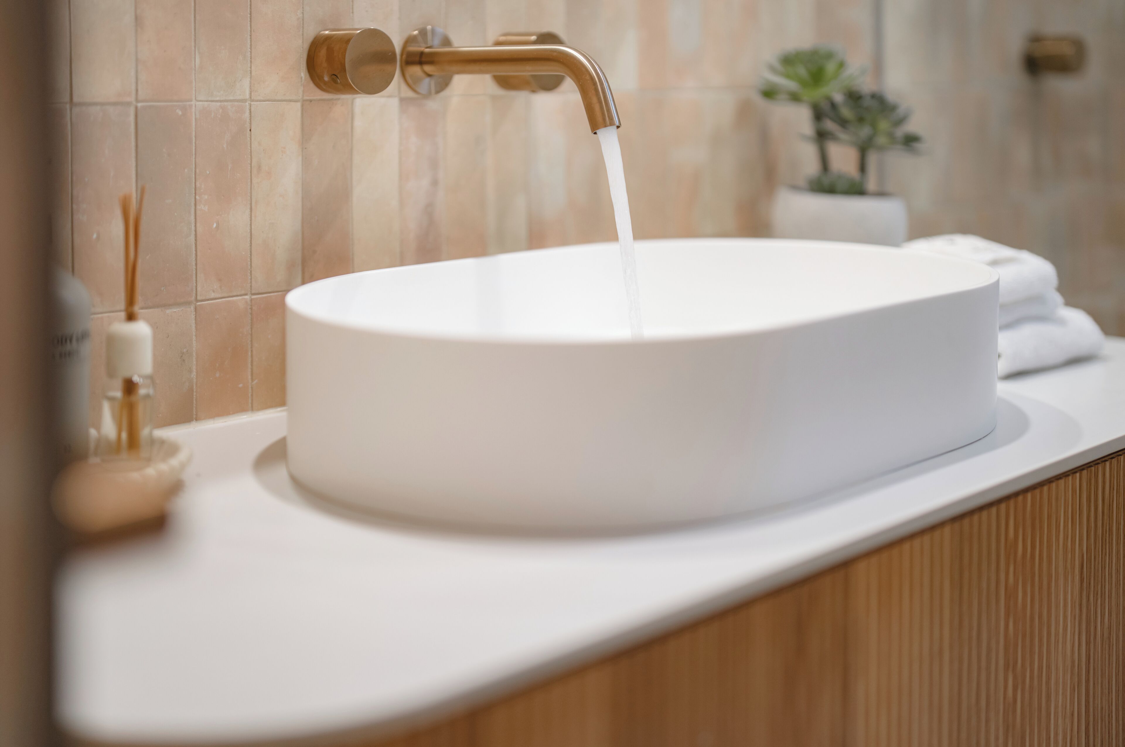 A bathroom with a white sink, a gold faucet, and a potted plant in the background.
