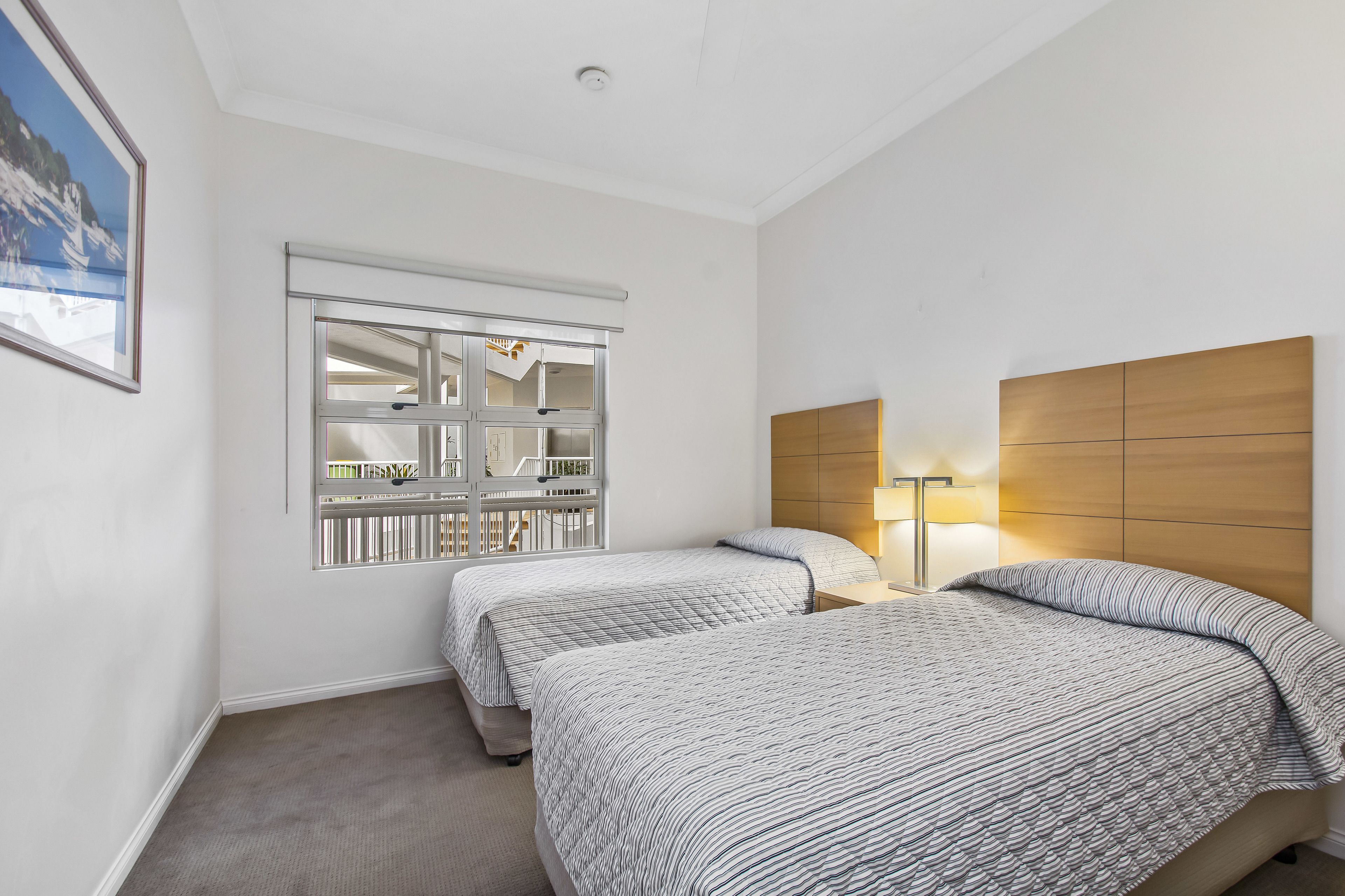 A hotel room with two beds, a window with a view of a balcony, and a wooden headboard.
