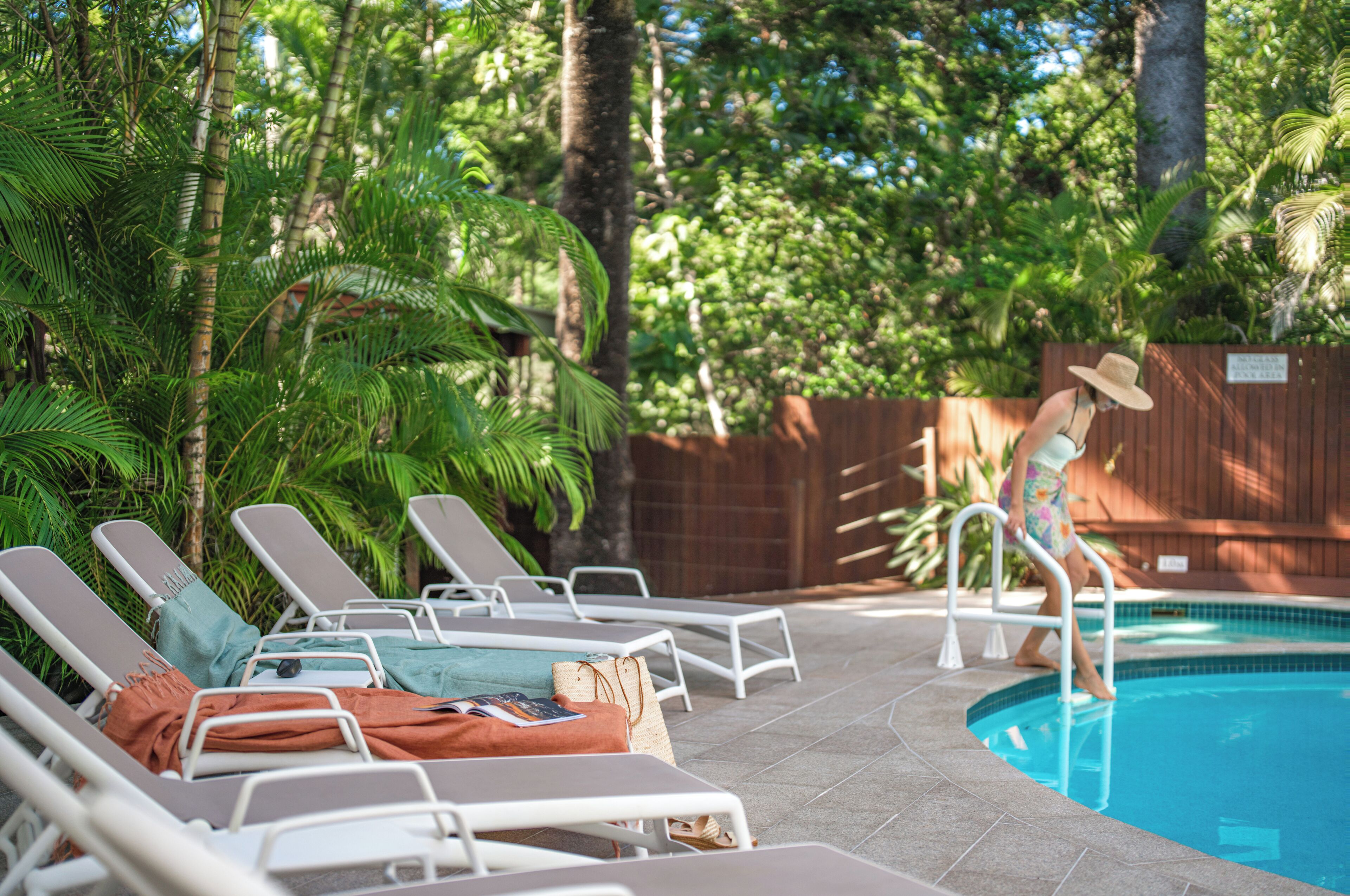 A poolside area with lounge chairs, a wooden fence, and lush greenery.
