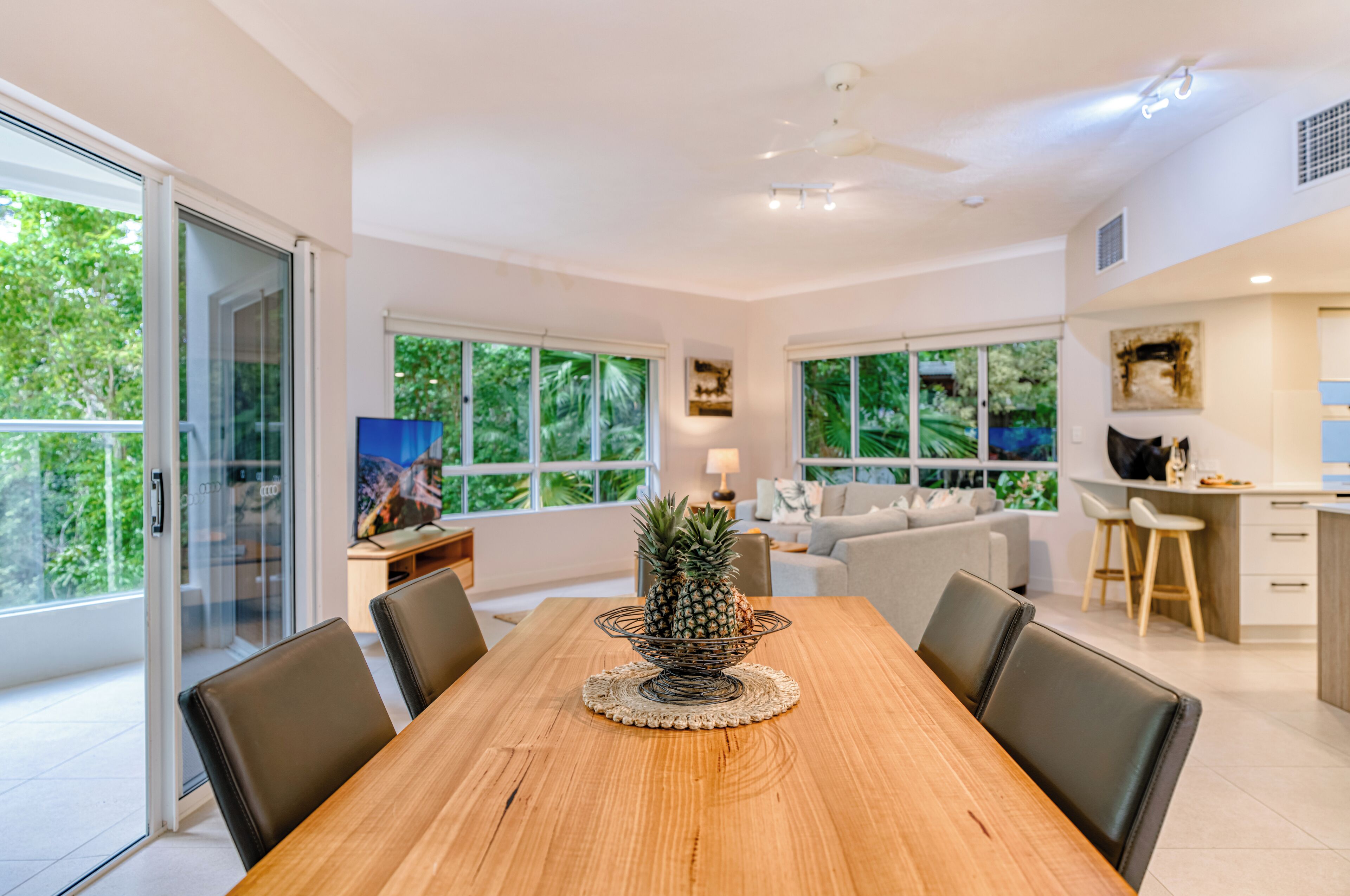 A modern dining area with a wooden table, black chairs, and a pineapple centerpiece.
