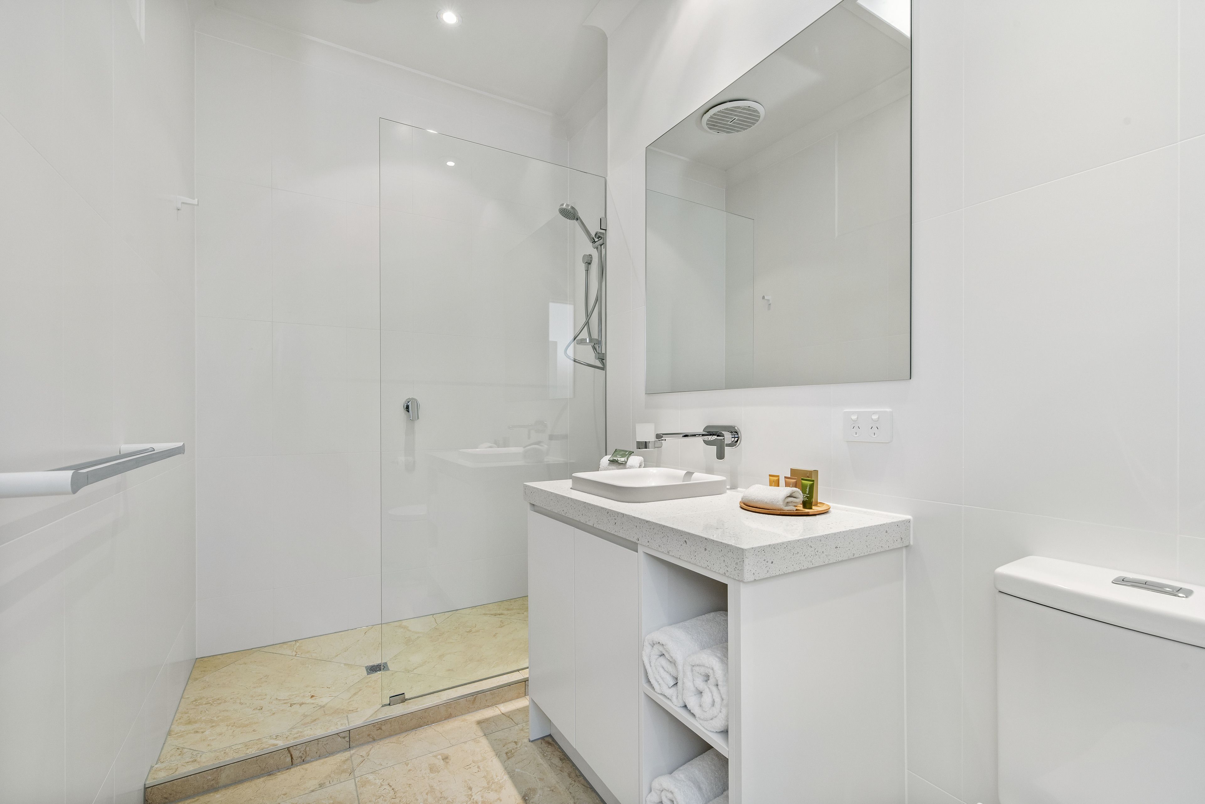 Un baño moderno con cabina de ducha acristalada, un lavabo con espejo y toallas ordenadas sobre una repisa.