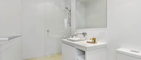 Un baño moderno con cabina de ducha acristalada, un lavabo con espejo y toallas ordenadas sobre una repisa.