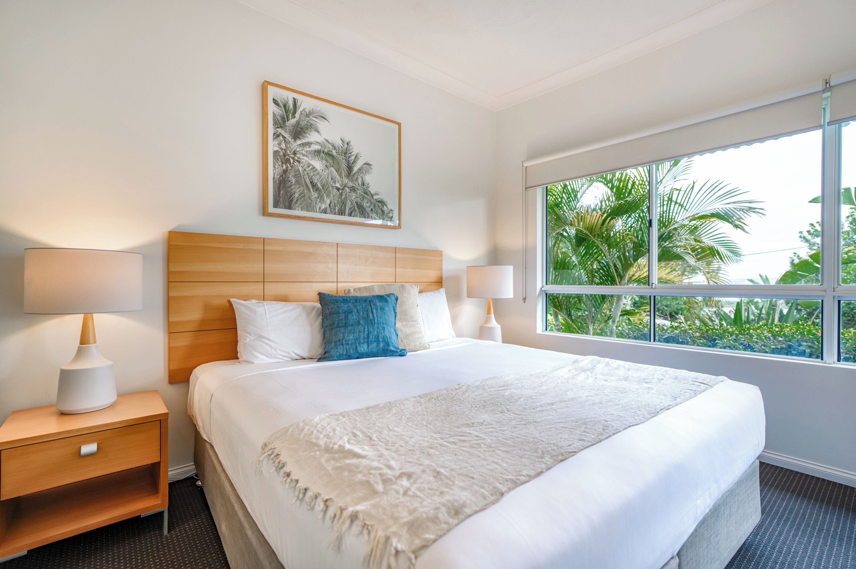 Habitación de hotel con cama, mesitas de noche, un ventanal con vistas a zonas verdes y un cuadro en la pared.