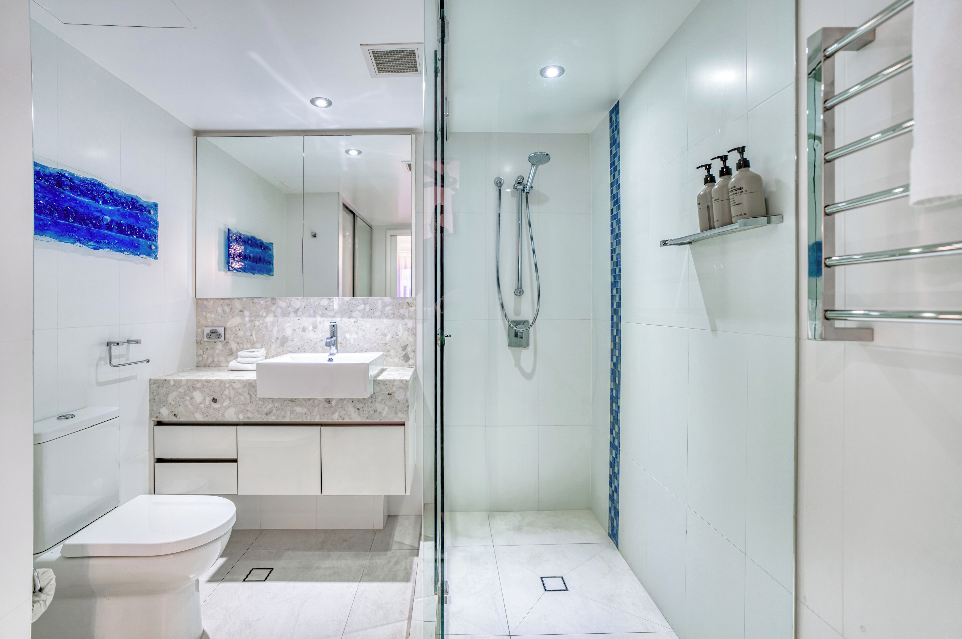 A modern bathroom with a glass-enclosed shower, a white sink, and a marble countertop.