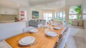 A modern dining area with a wooden table set for four, white plates, and a bottle of water. - The Lookout Resort (Noosa Heads)