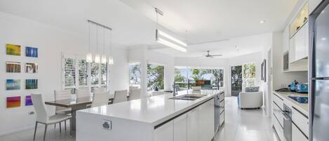 A modern kitchen with white cabinetry, a central island, and a dining area with a white table and chairs.