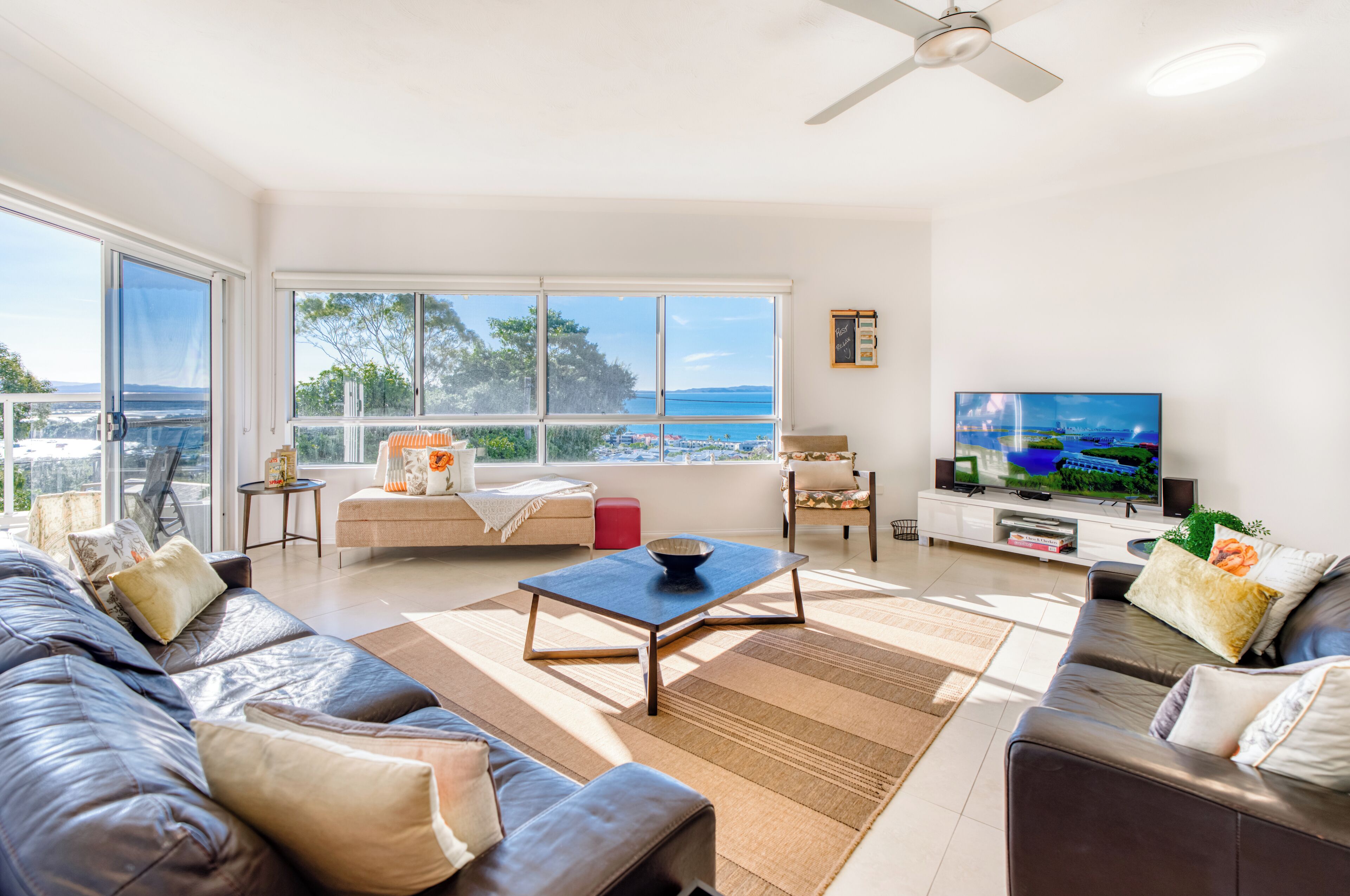 A spacious living room with a large window offering a view of the sea, a flat-screen TV, and a comfortable seating area.